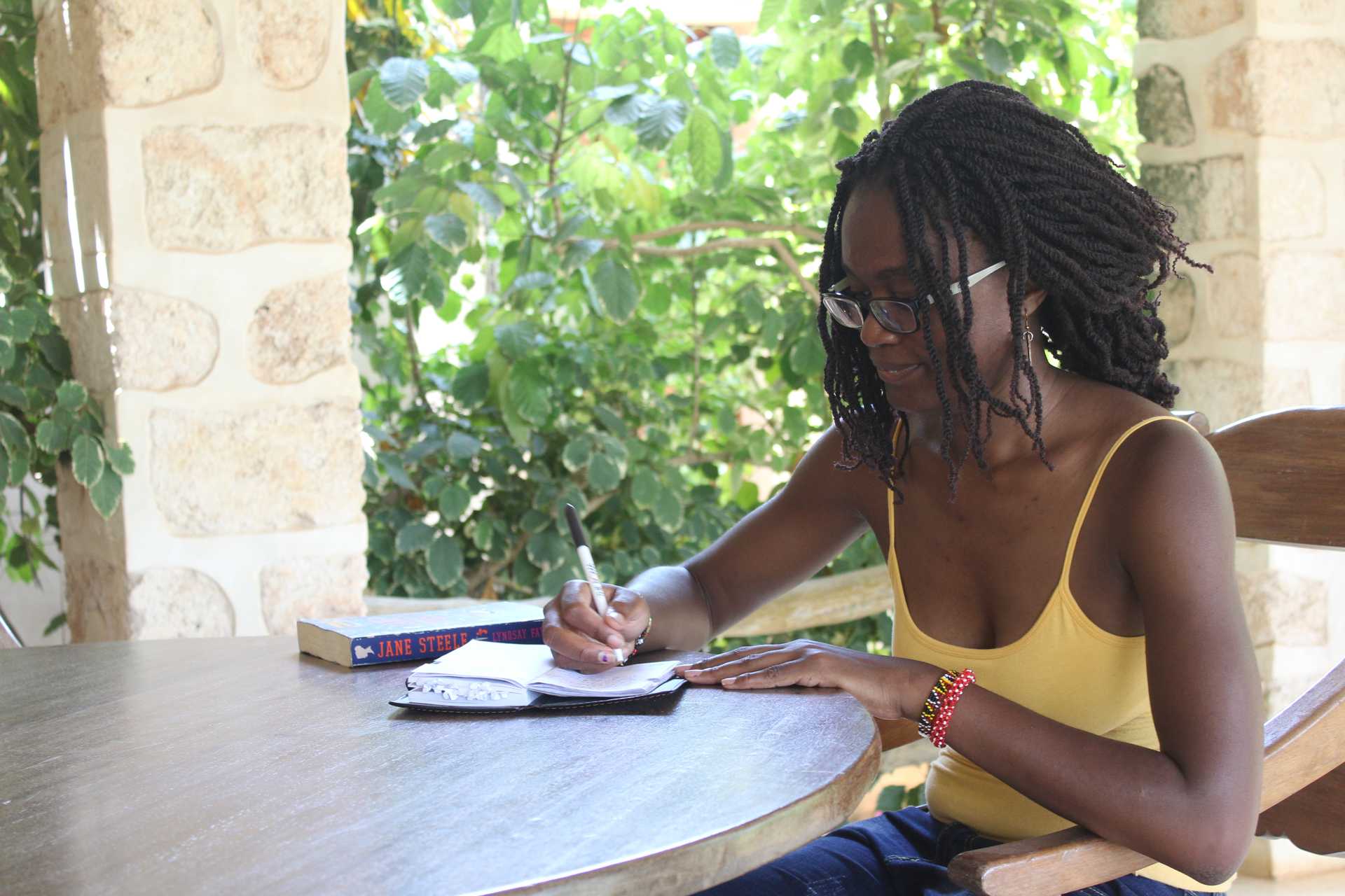 Harriet Owalla writing at a table in Lonno Lodge